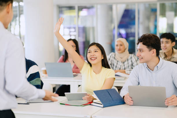 happy  student raising arm to answer question while attending class with her university colleagues. - 教育 個(gè)照片及圖片檔